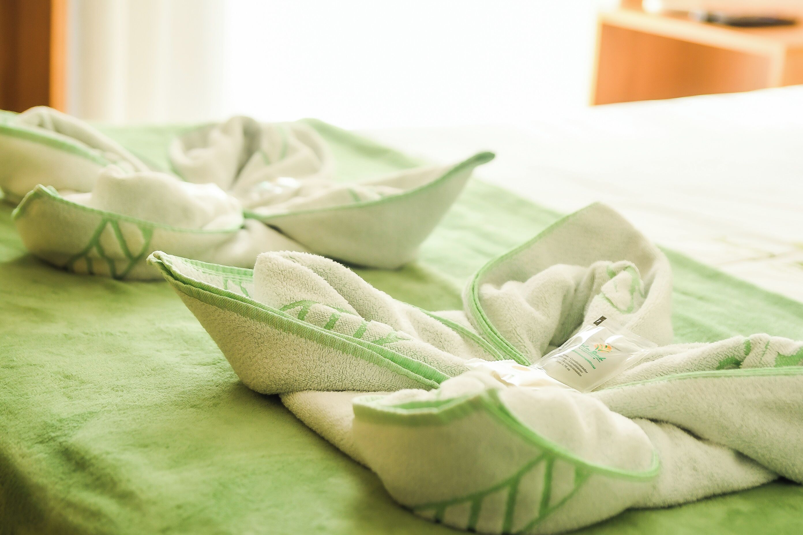 Una cama con una manta verde y toallas dobladas en forma de barco.