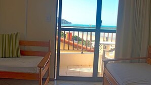 Una habitación con dos camas de madera, un ventanal corredero que da a un balcón con vistas a la playa y al océano.