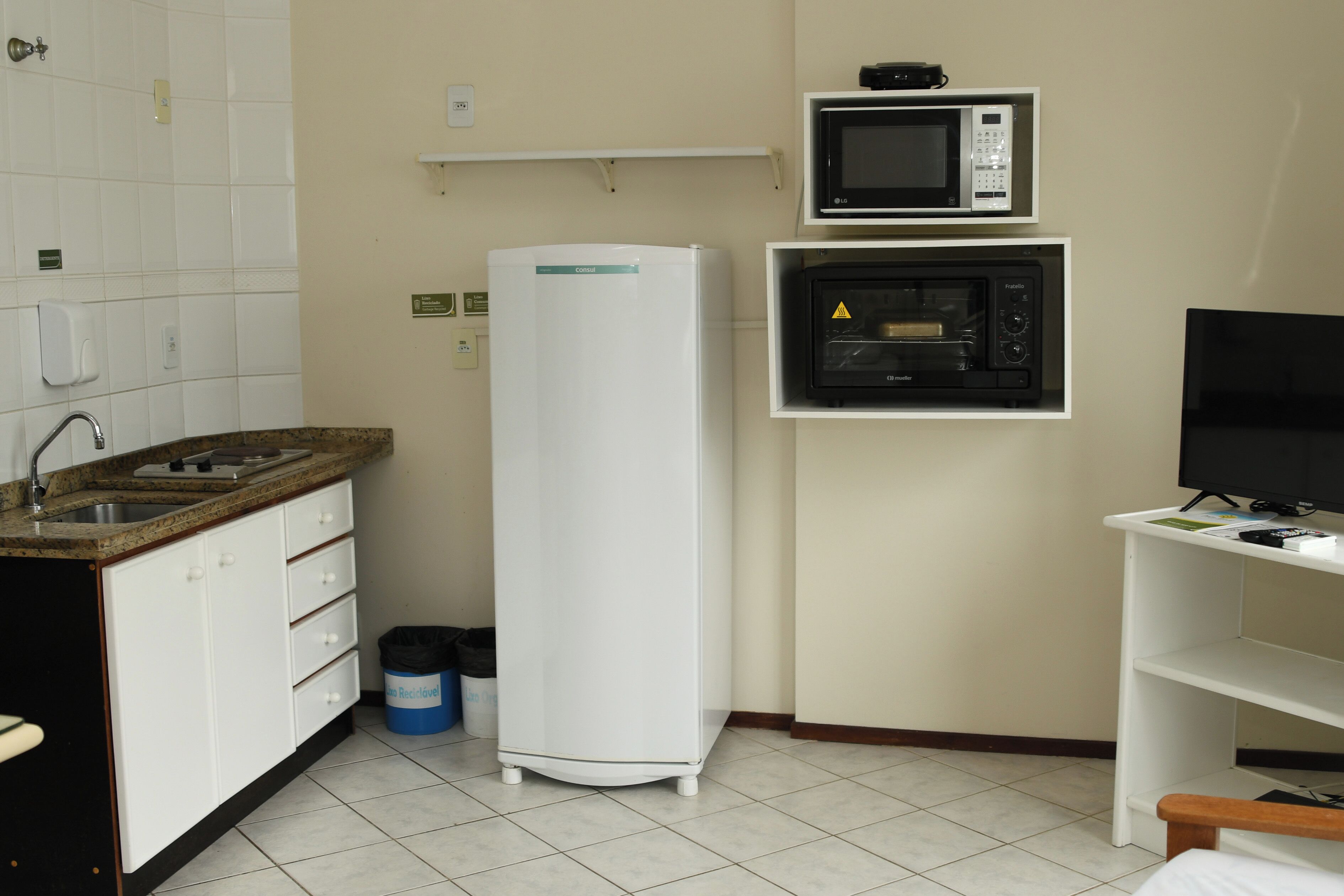 A compact kitchen with a refrigerator, microwave, and a TV on a shelf.