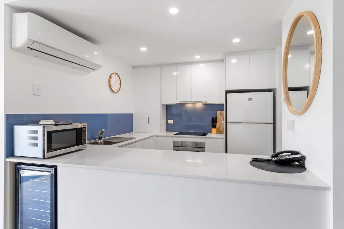 A modern kitchen with white cabinetry, a built-in microwave, a refrigerator, and a phone on the counter.
