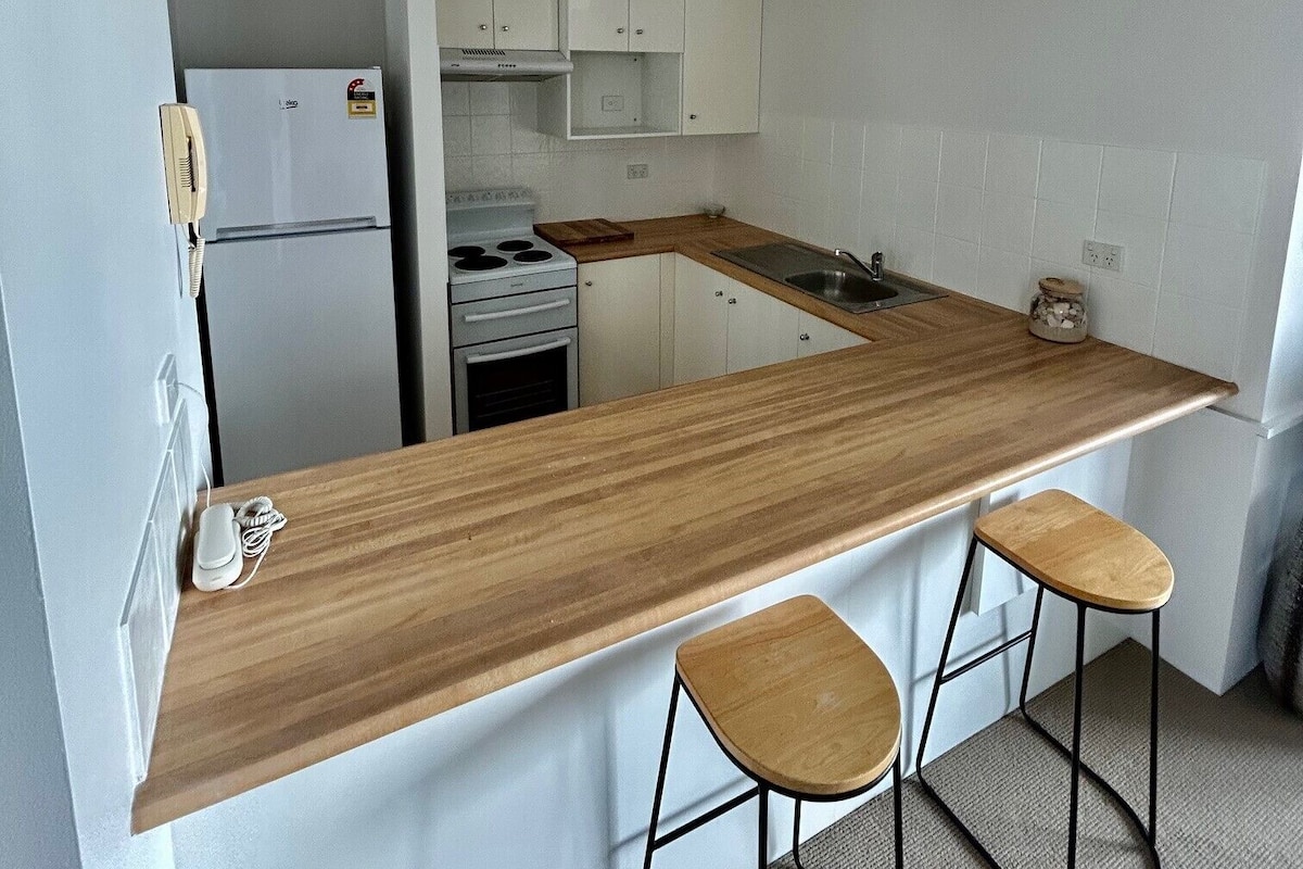 A compact kitchen with a wooden countertop, white cabinets, a built-in stove, and a small sink.