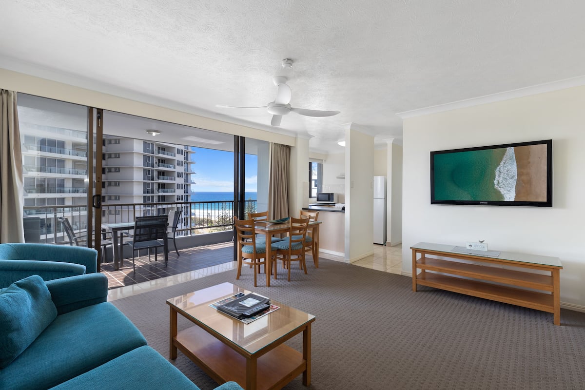 A hotel room with a balcony, a dining area, a TV, and a sofa.