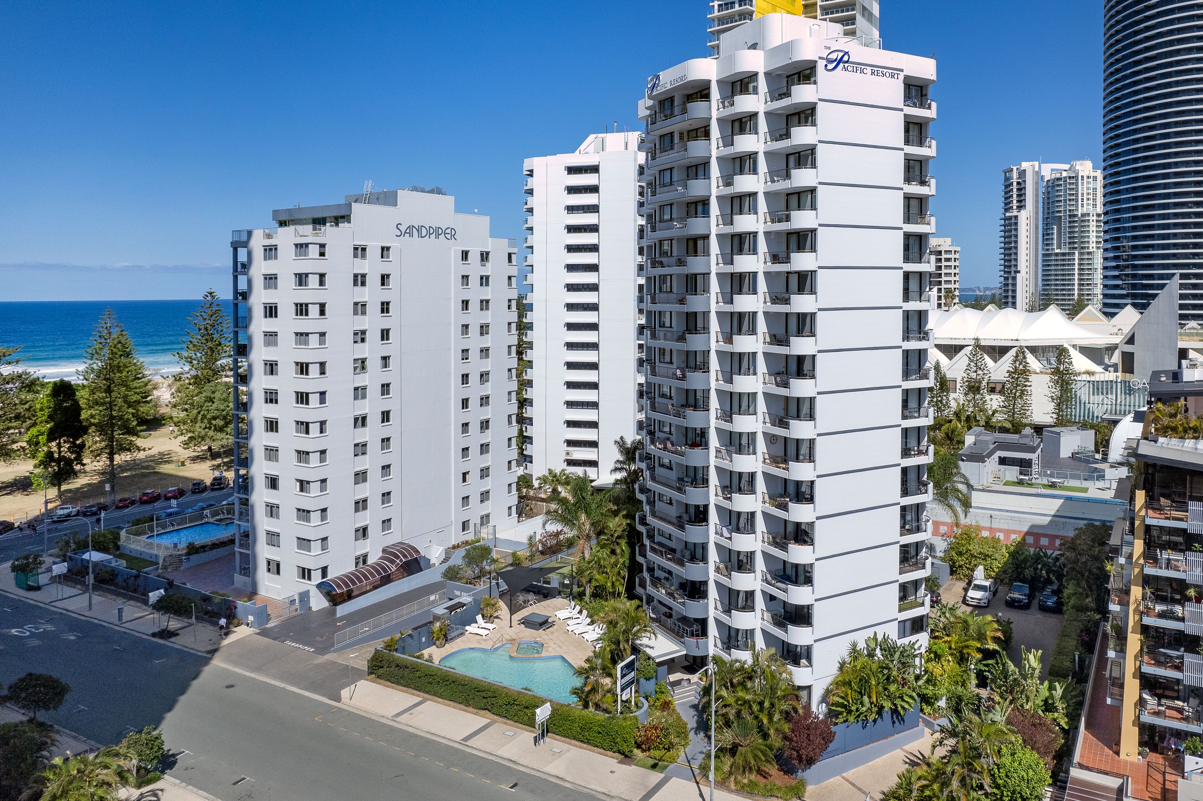 A high-rise hotel with multiple floors, a swimming pool, and a view of the ocean.