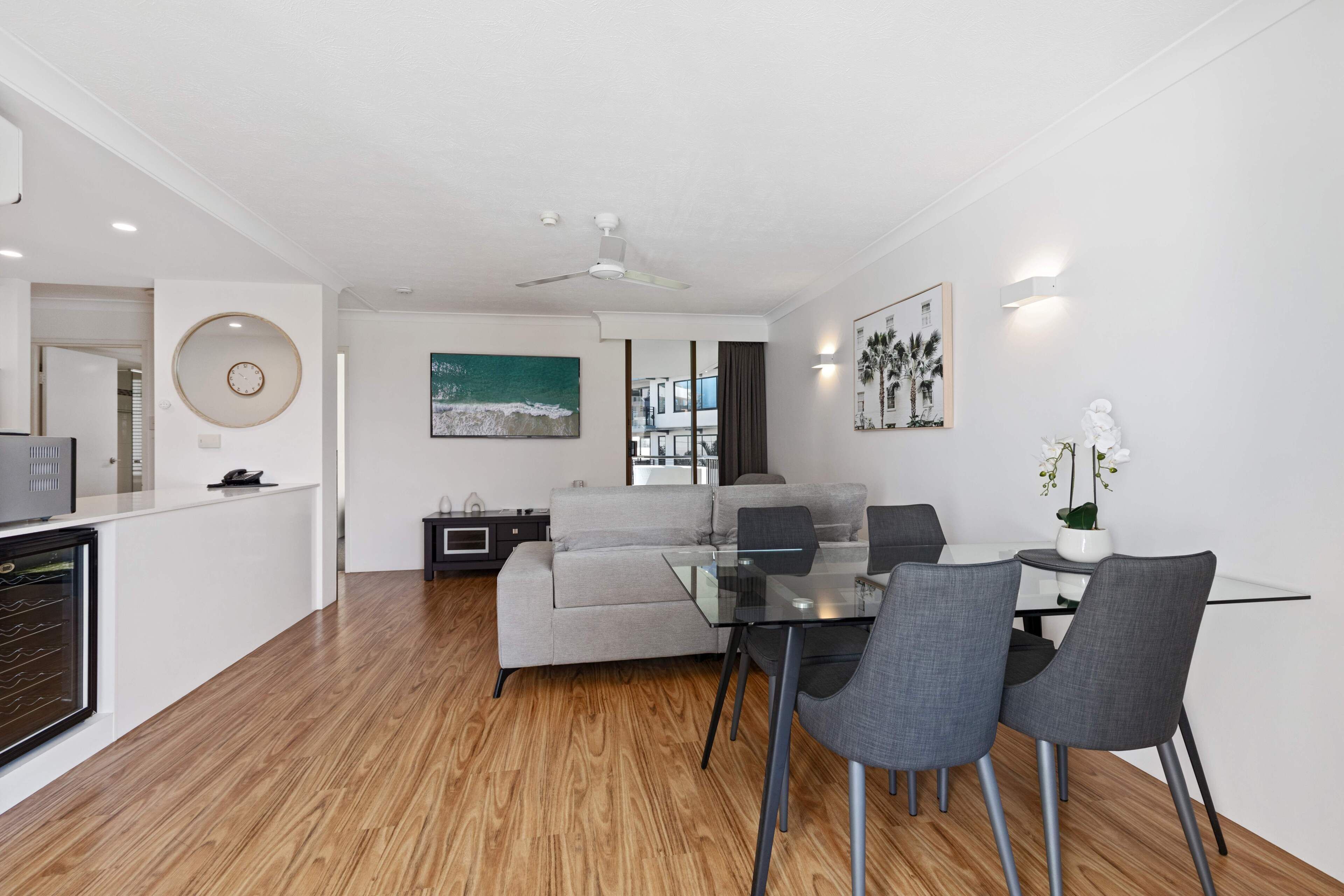 Un salon moderne avec une table à manger en verre, un canapé gris et un ventilateur de plafond.