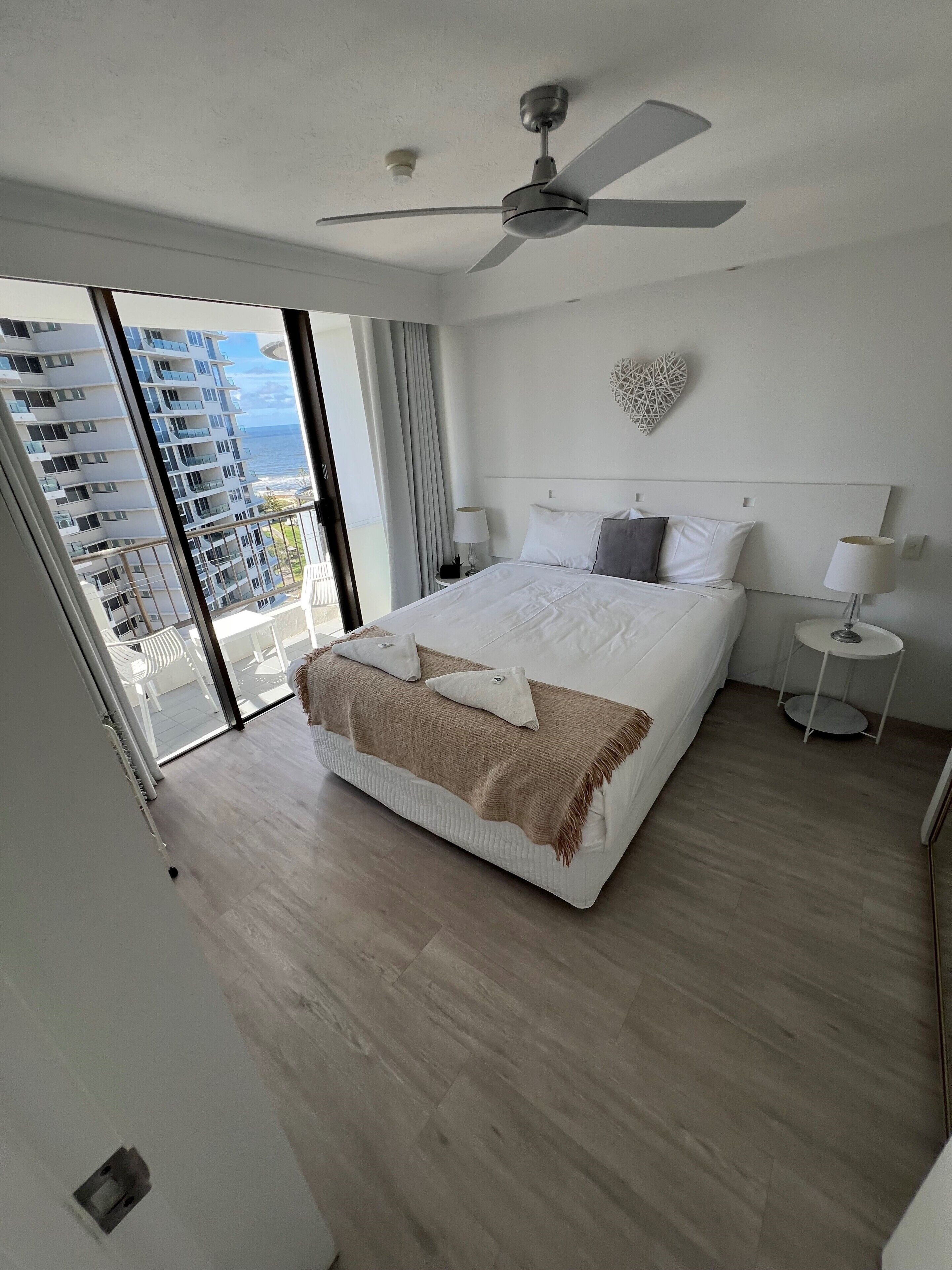 Een moderne hotelkamer met een groot bed, een plafondventilator, uitzicht op de oceaan en een balkon.