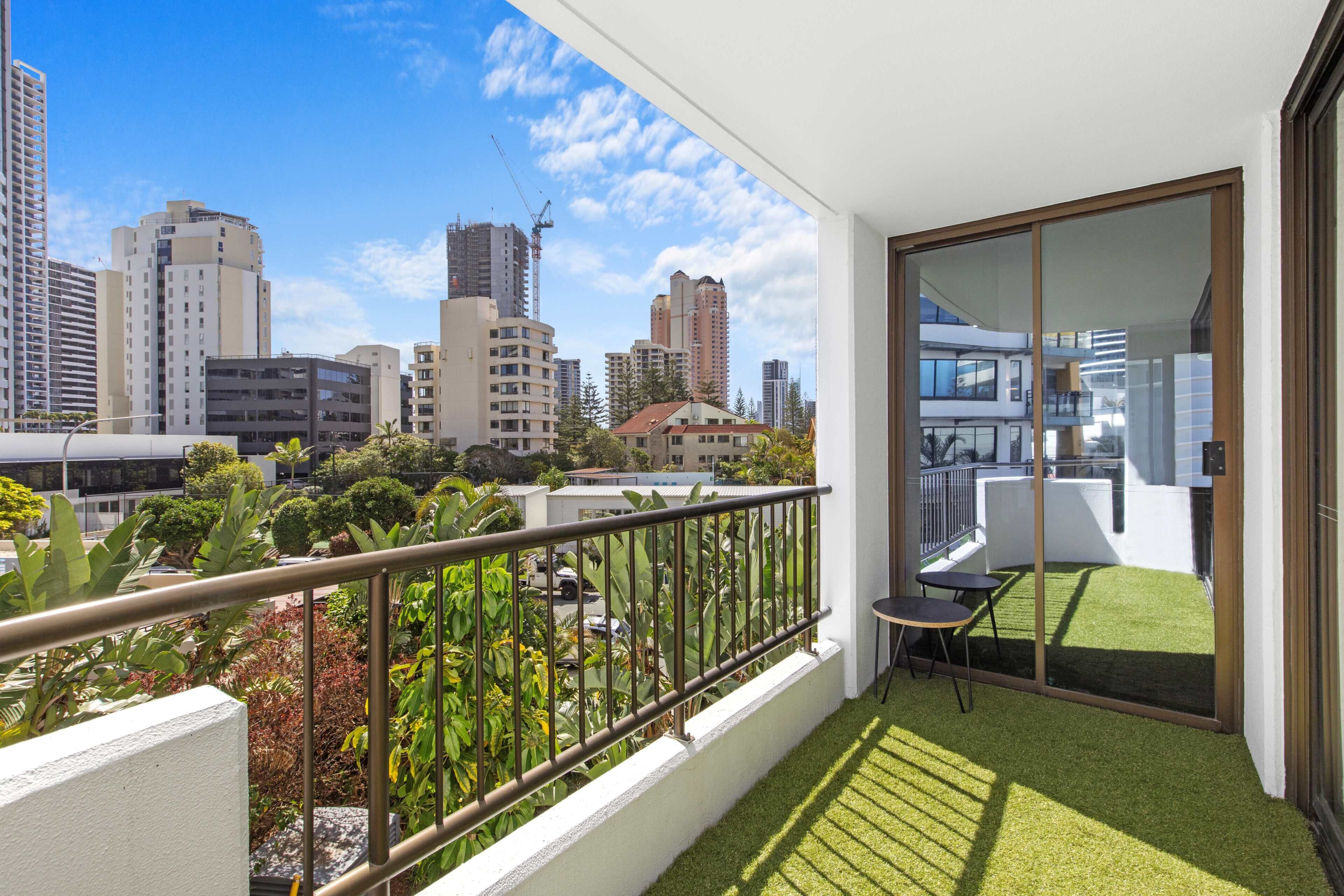 Un balcón con vista a un paisaje urbano, una pequeña mesa y césped artificial.