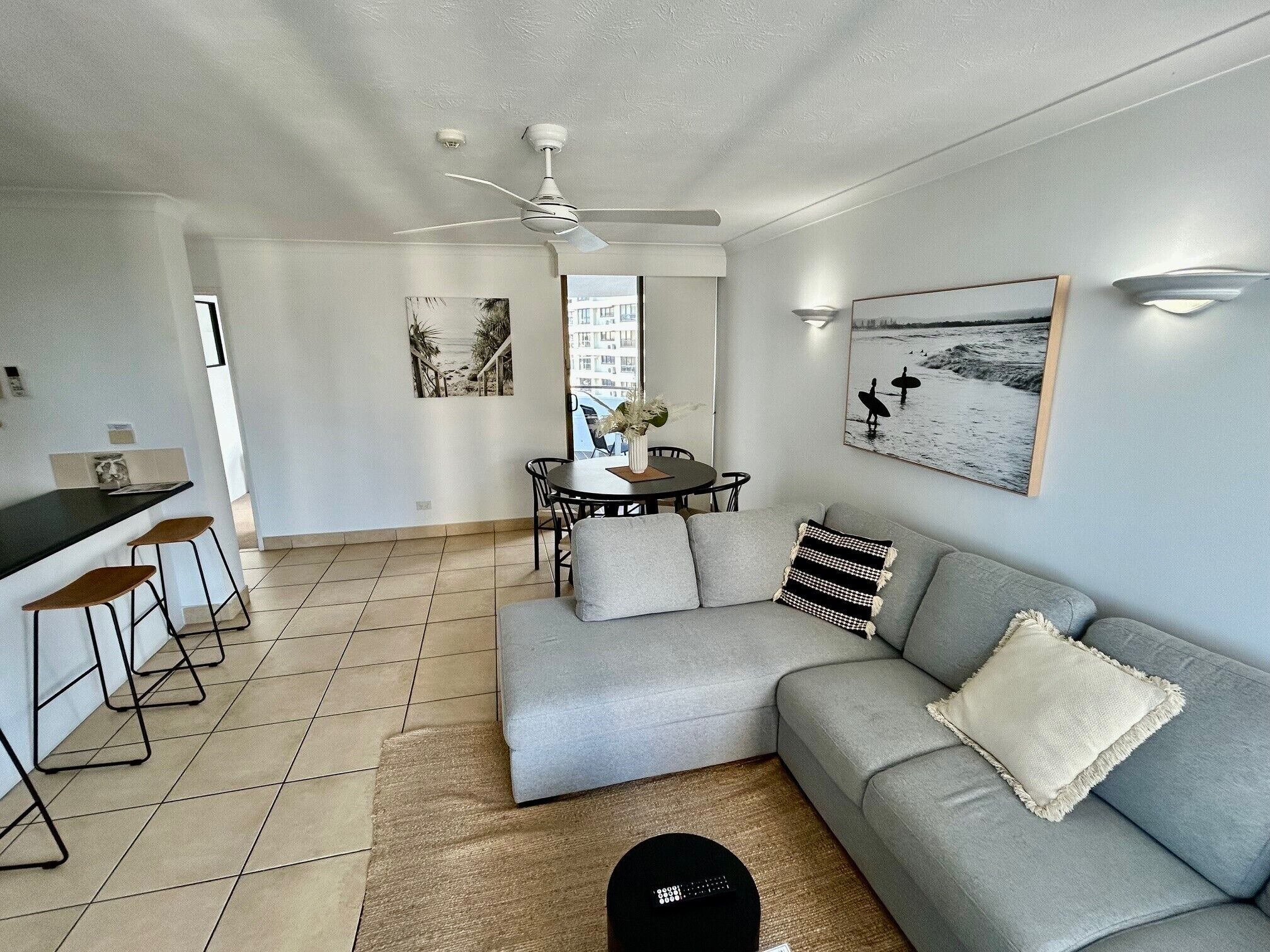A modern living room with a grey sofa, a dining table with chairs, a ceiling fan, and artwork on the walls.