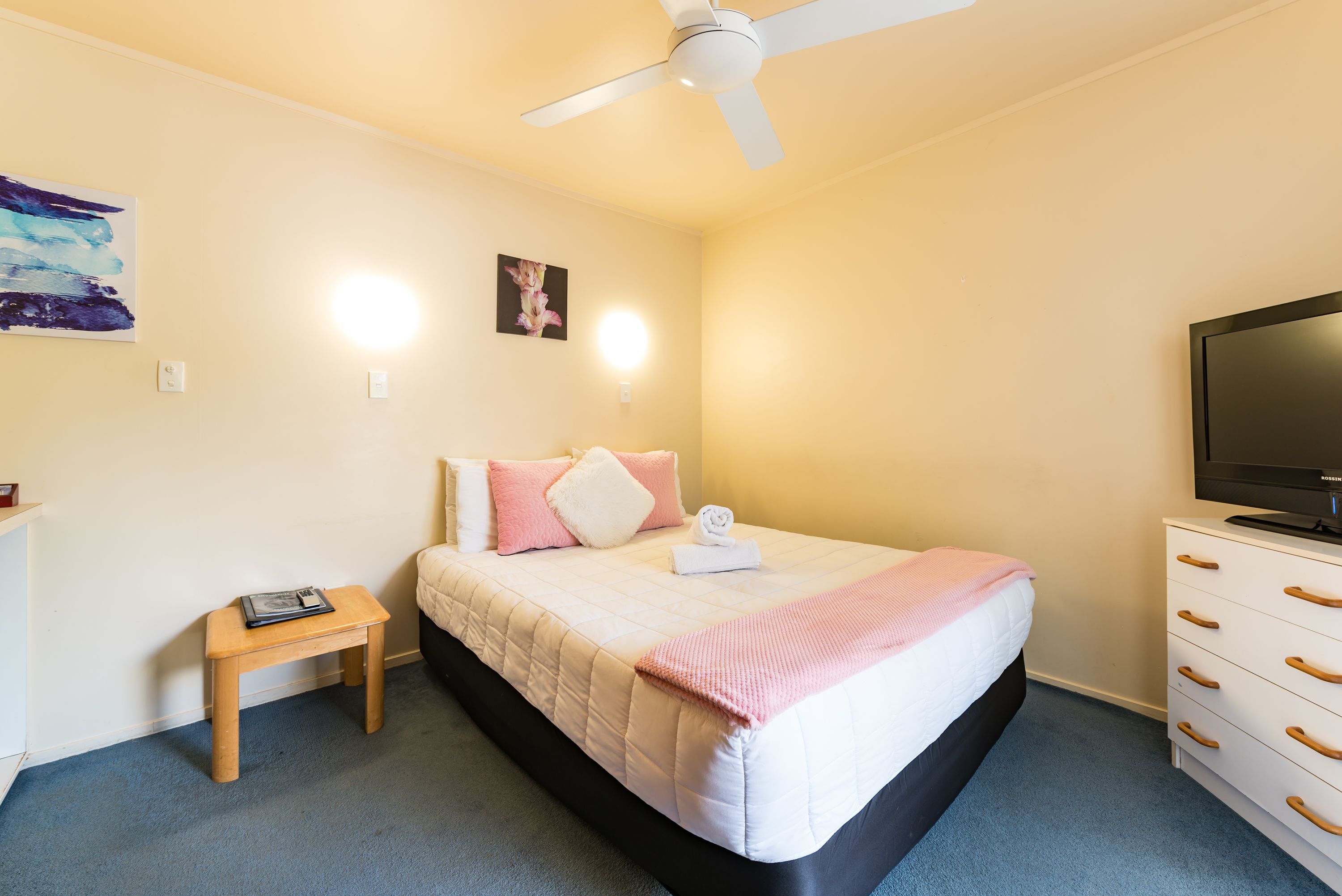 A bedroom with a bed, a nightstand, a TV, and a ceiling fan.
