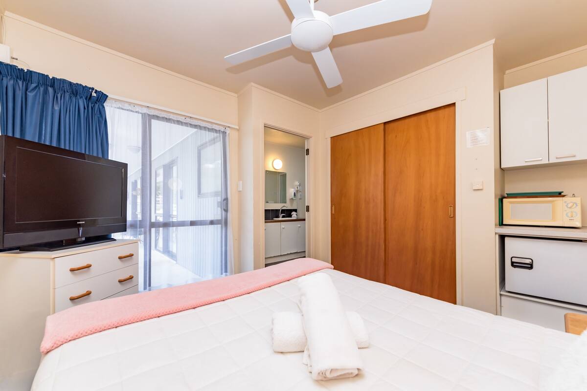 A hotel room with a bed, a television, a wardrobe, a microwave, and a bathroom visible through an open door.
