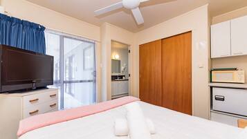 Habitación de hotel con cama, televisor, armario, microondas y baño visible a través de una puerta abierta.