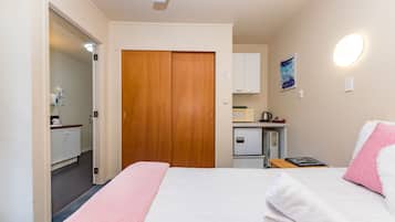 A hotel room with a bed, a wooden wardrobe, a kitchenette, and a bathroom visible through an open door.