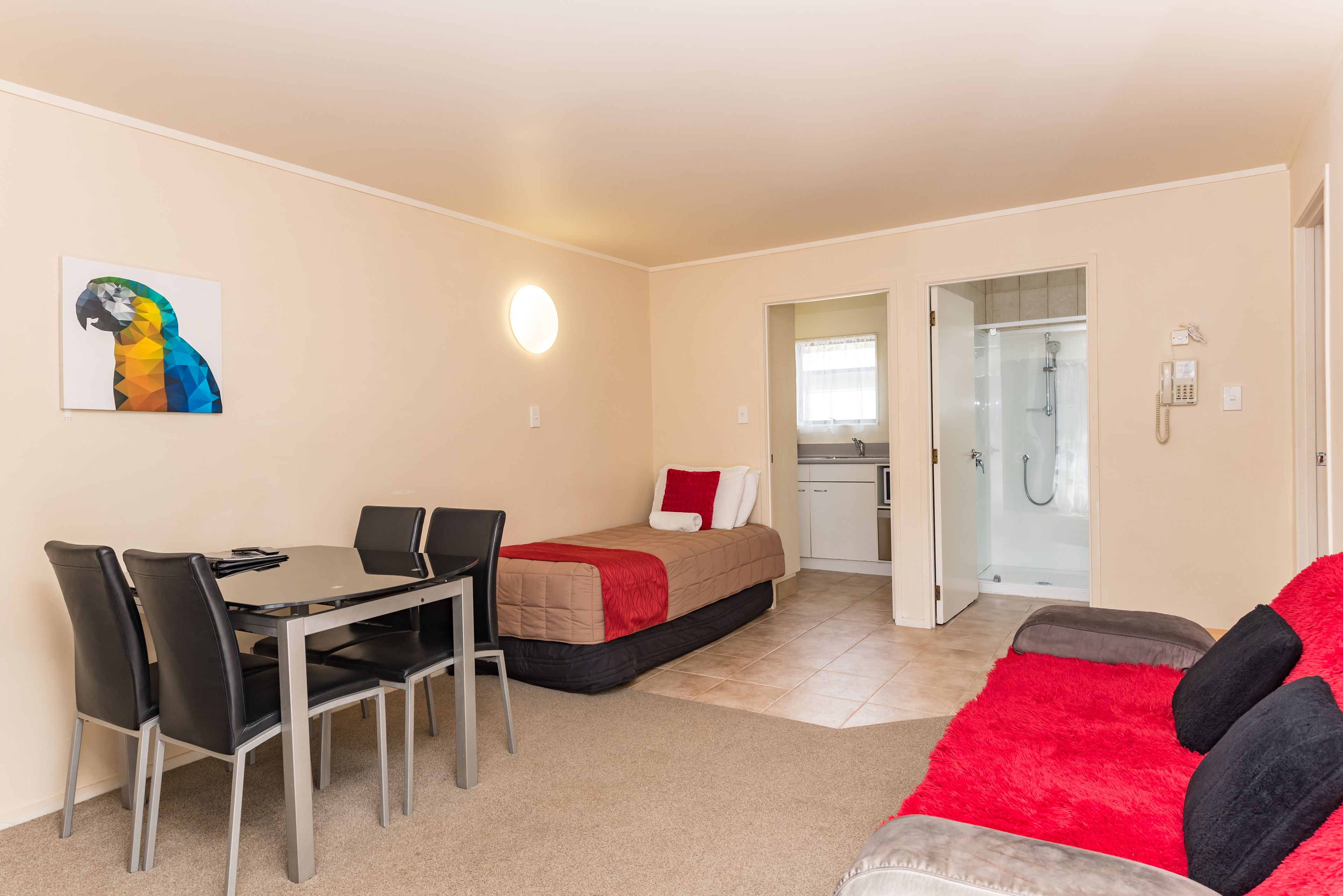 A compact hotel room with a dining area, a bed, a shower, and a phone on the wall.