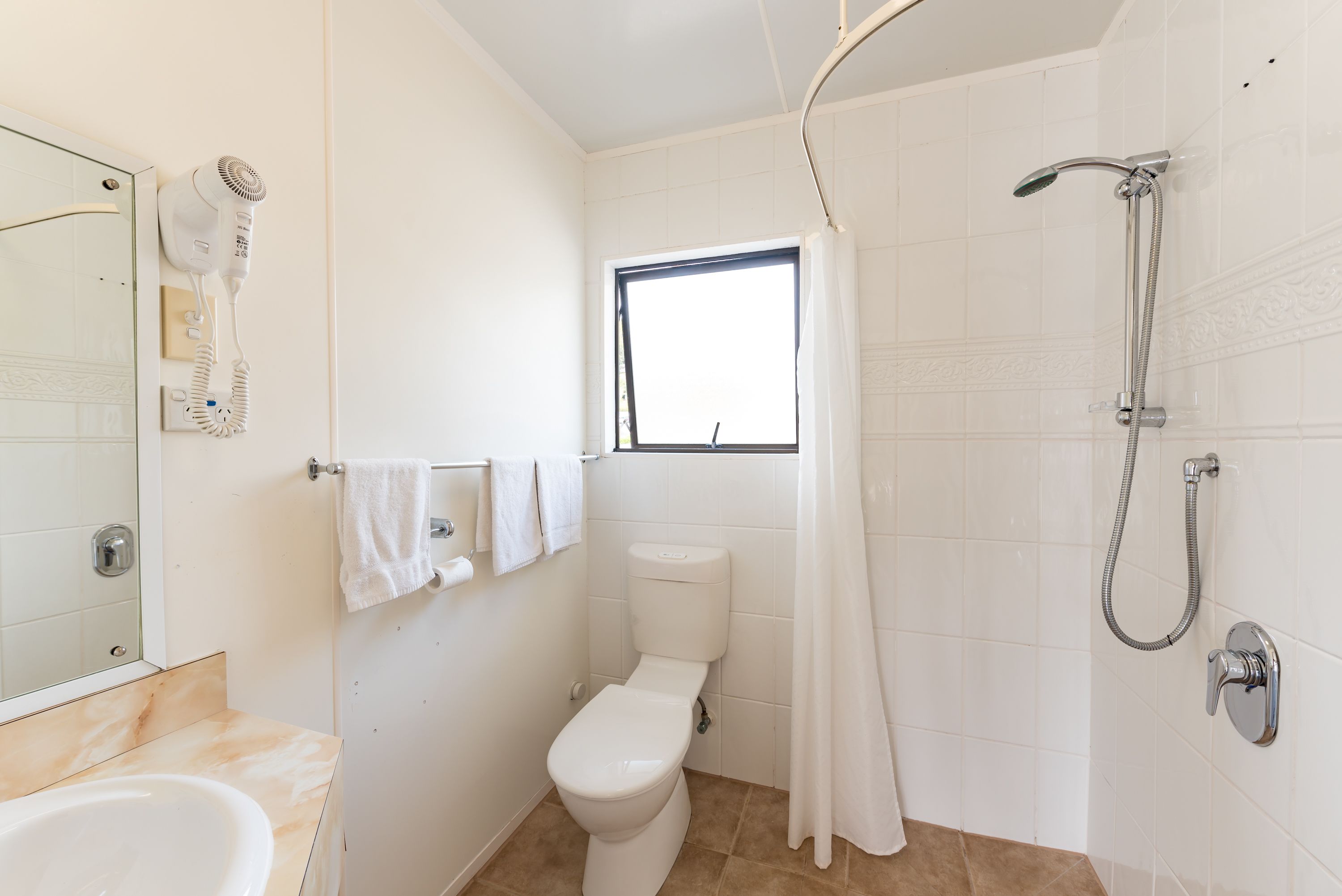 Casa de banho com sanita, lavatório, secador de cabelo, chuveiro e janela.