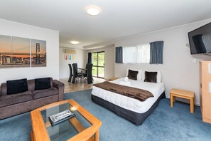 A hotel room with a bed, a sofa, a coffee table, a TV, and a cityscape painting. - Dolphin Motel (Paihia)