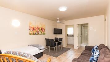 Uma sala de estar moderna com uma cama, um sofá, uma mesa de jantar com cadeiras, uma televisão e um ventilador de teto.
