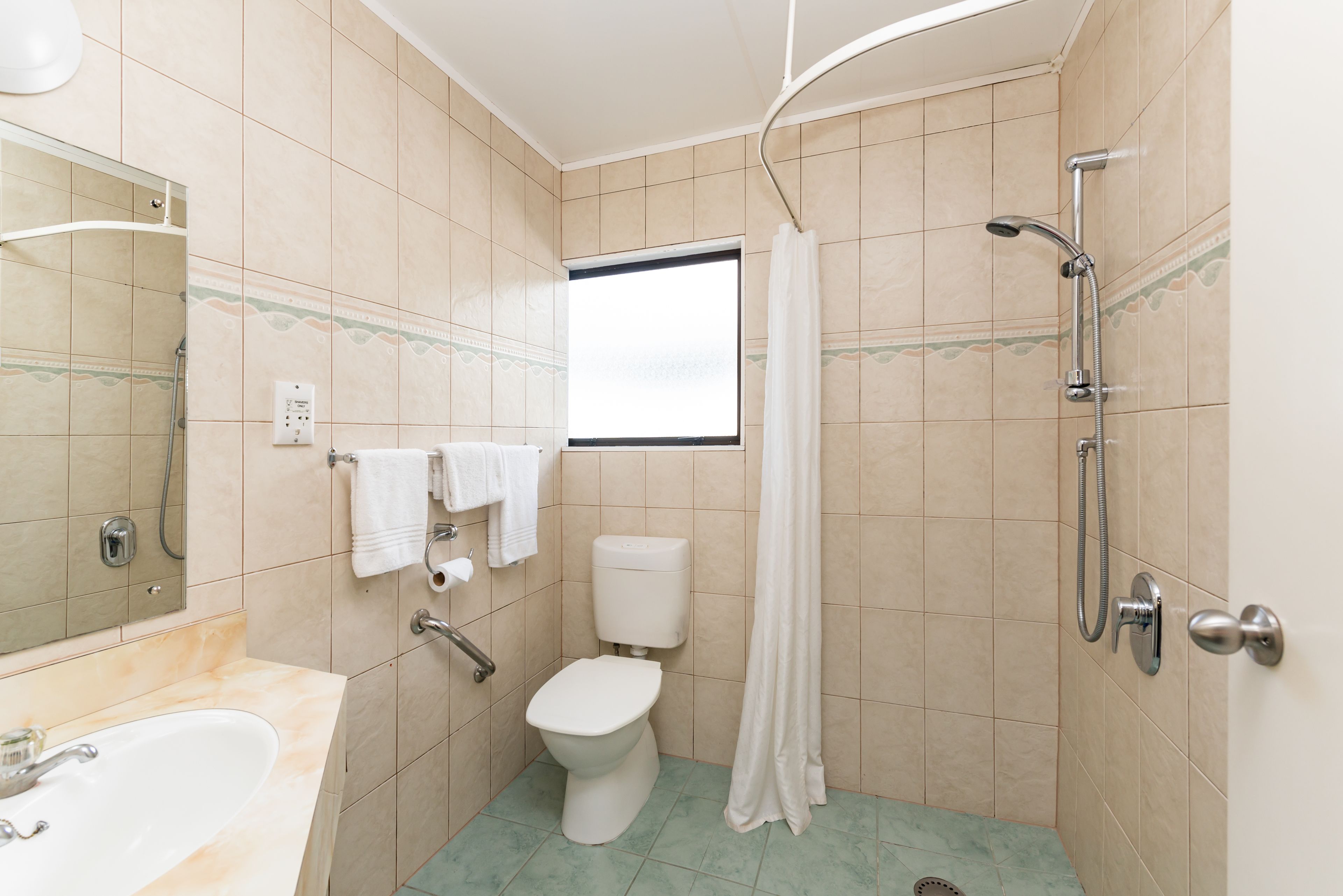 A bathroom with a toilet, sink, shower, and a window.