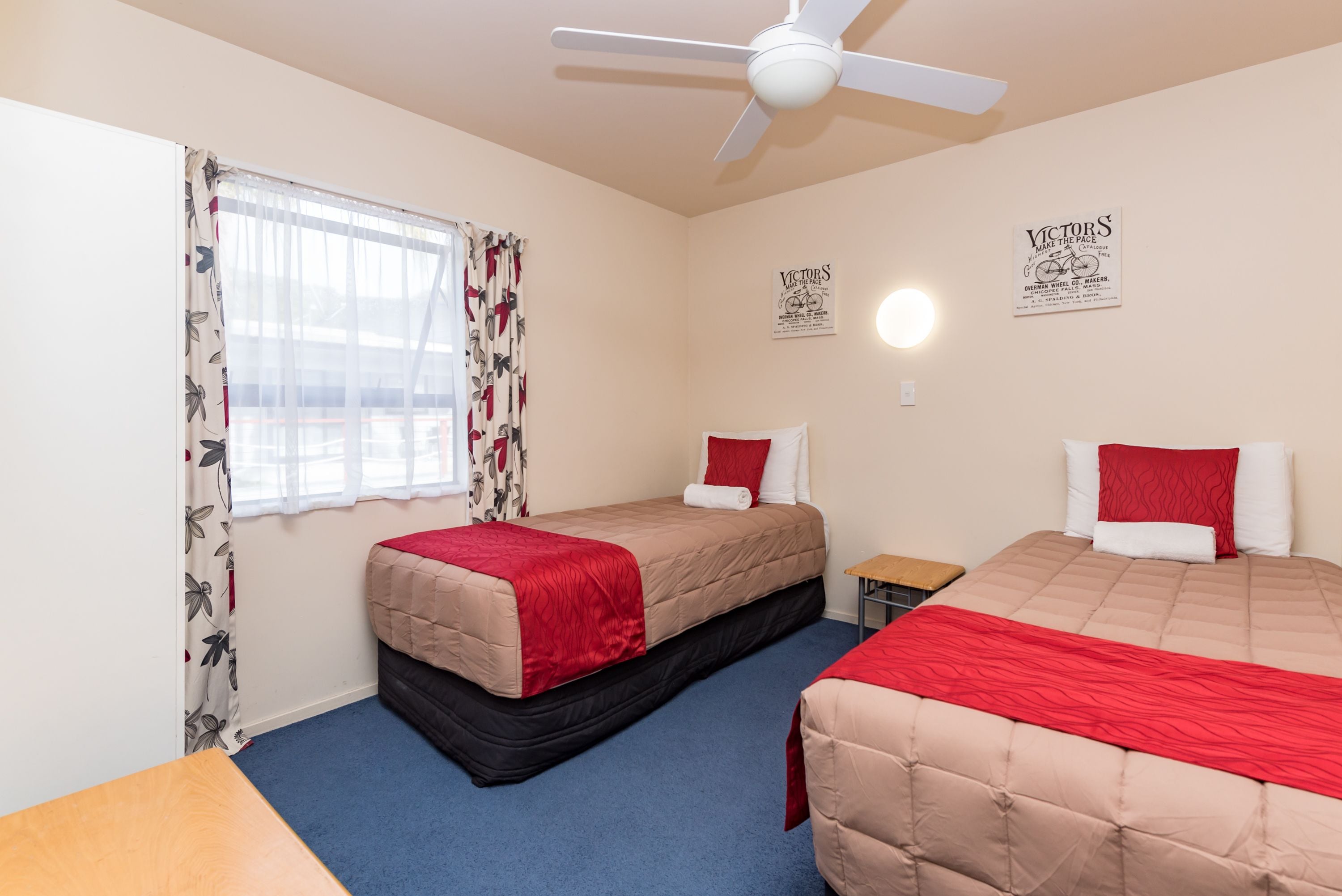 A bedroom with two beds, a ceiling fan, and a window with floral curtains.