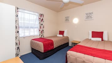 A bedroom with two beds, a ceiling fan, and a window with floral curtains.