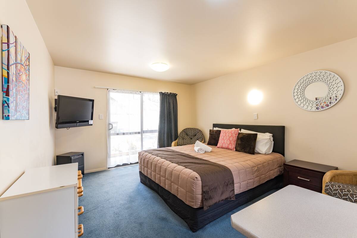 A hotel room with a bed, a desk, a television, and a large window with curtains.