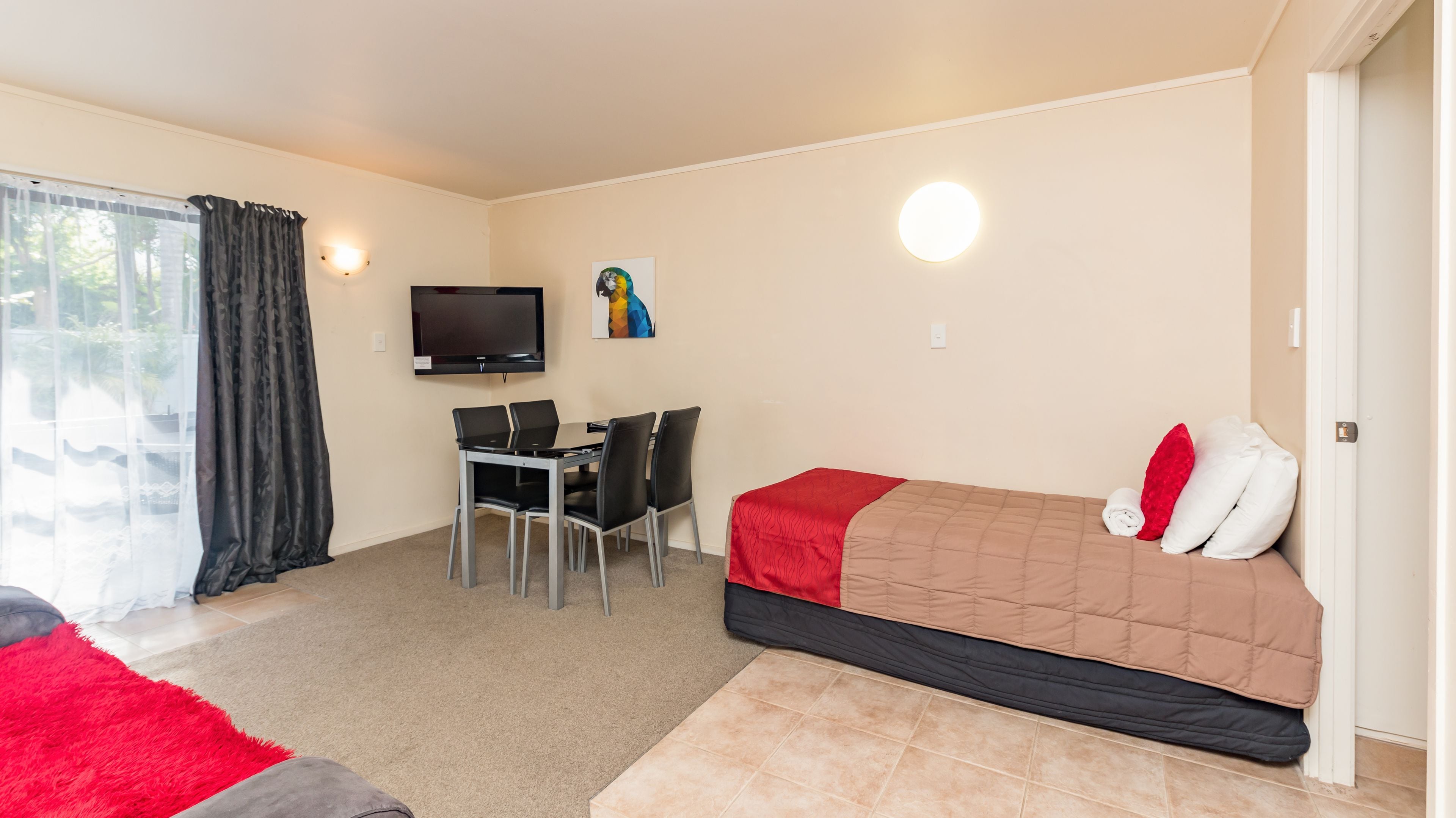 Una habitación de hotel pequeña con cama, escritorio con sillas, televisor y ventana con cortinas.