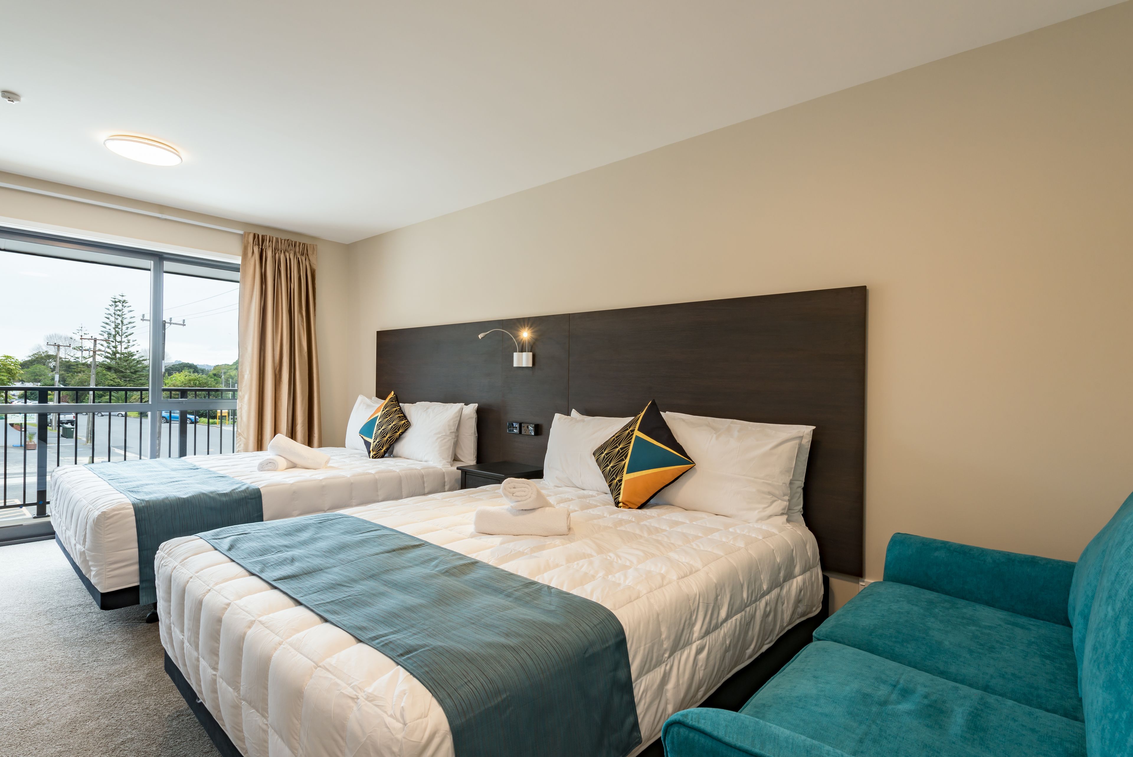 A hotel room with two beds, a balcony, and a teal armchair.