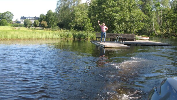 A person standing on a dock extending into a body of water, surrounded by greenery and trees. - Sikfors Herrgård (Hallefors)