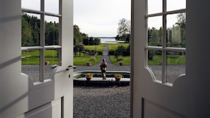 A view through a doorway with a gravel path leading to a grassy area and a body of water. - Sikfors Herrgård (Hallefors)