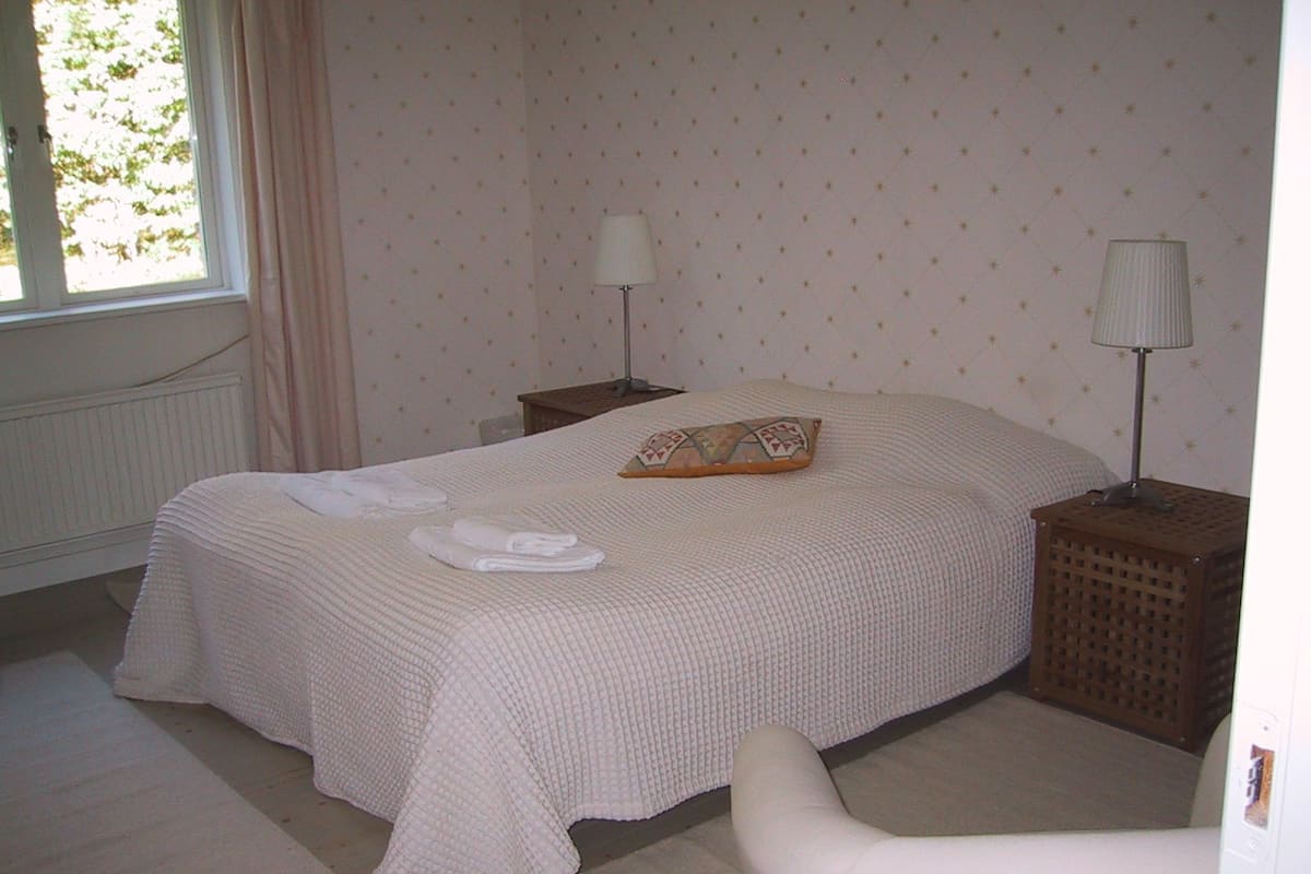 A neatly made bed with a pillow and folded towels, a bedside lamp, and a nightstand.