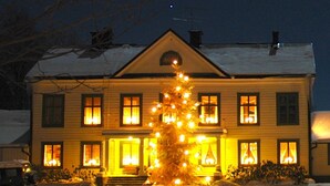 A two-story house with a snow-covered front yard and a lit Christmas tree. - Sikfors Herrgård (Hallefors)