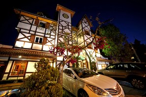 A traditional building with a clock tower, a car parked in front, and a tree with pink flowers. - Pousada Villaggio Italia (Campos do Jordão)