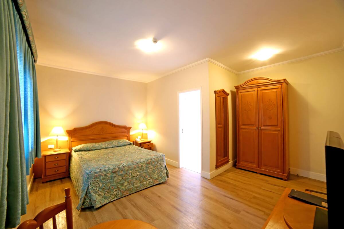 Ein Schlafzimmer mit einem Bett, zwei Nachttischen mit Lampen, einem Holzschrank und einem Fernseher.