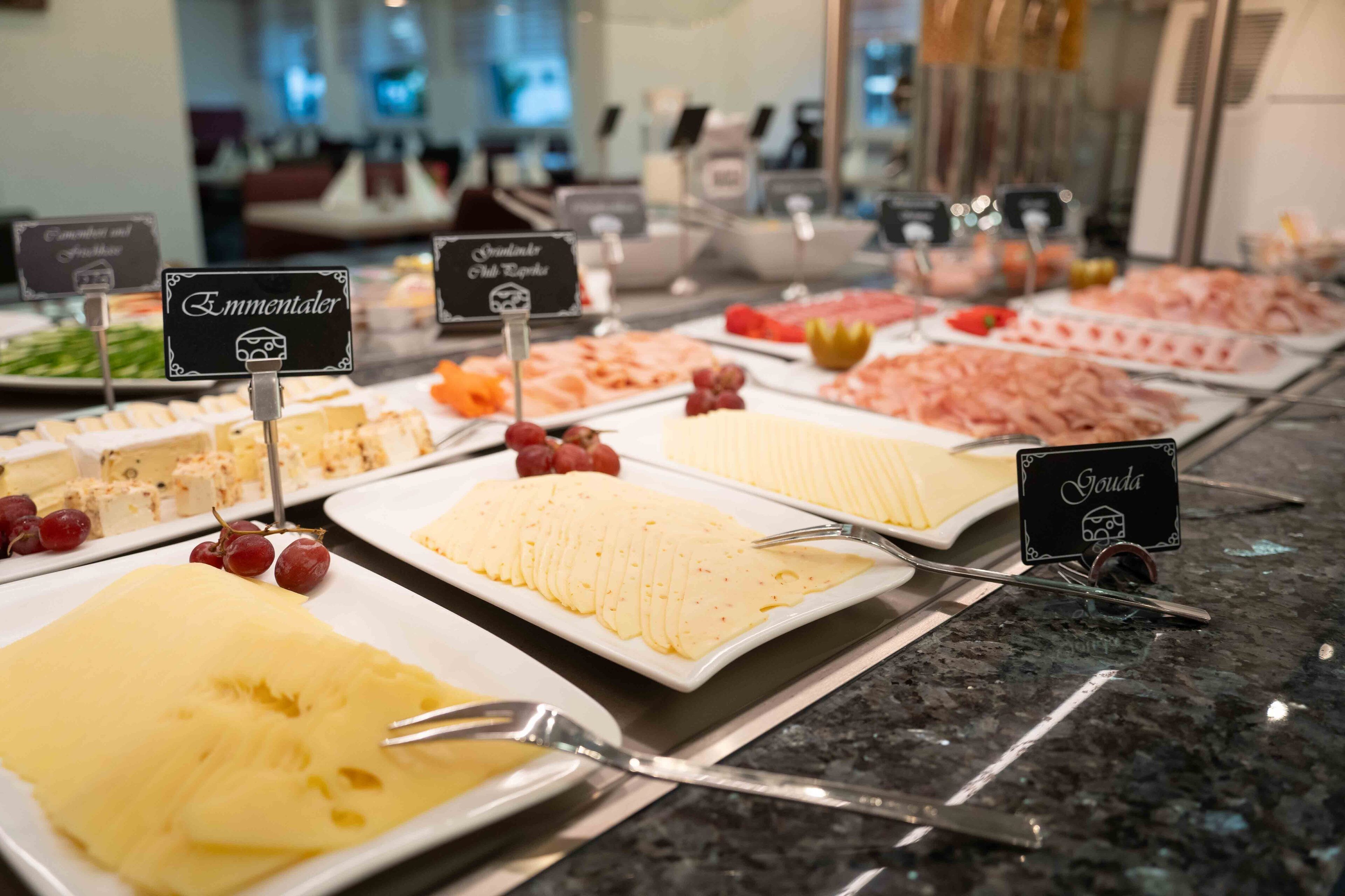A buffet with various cheese and meat platters, garnished with grapes and other fruits.
