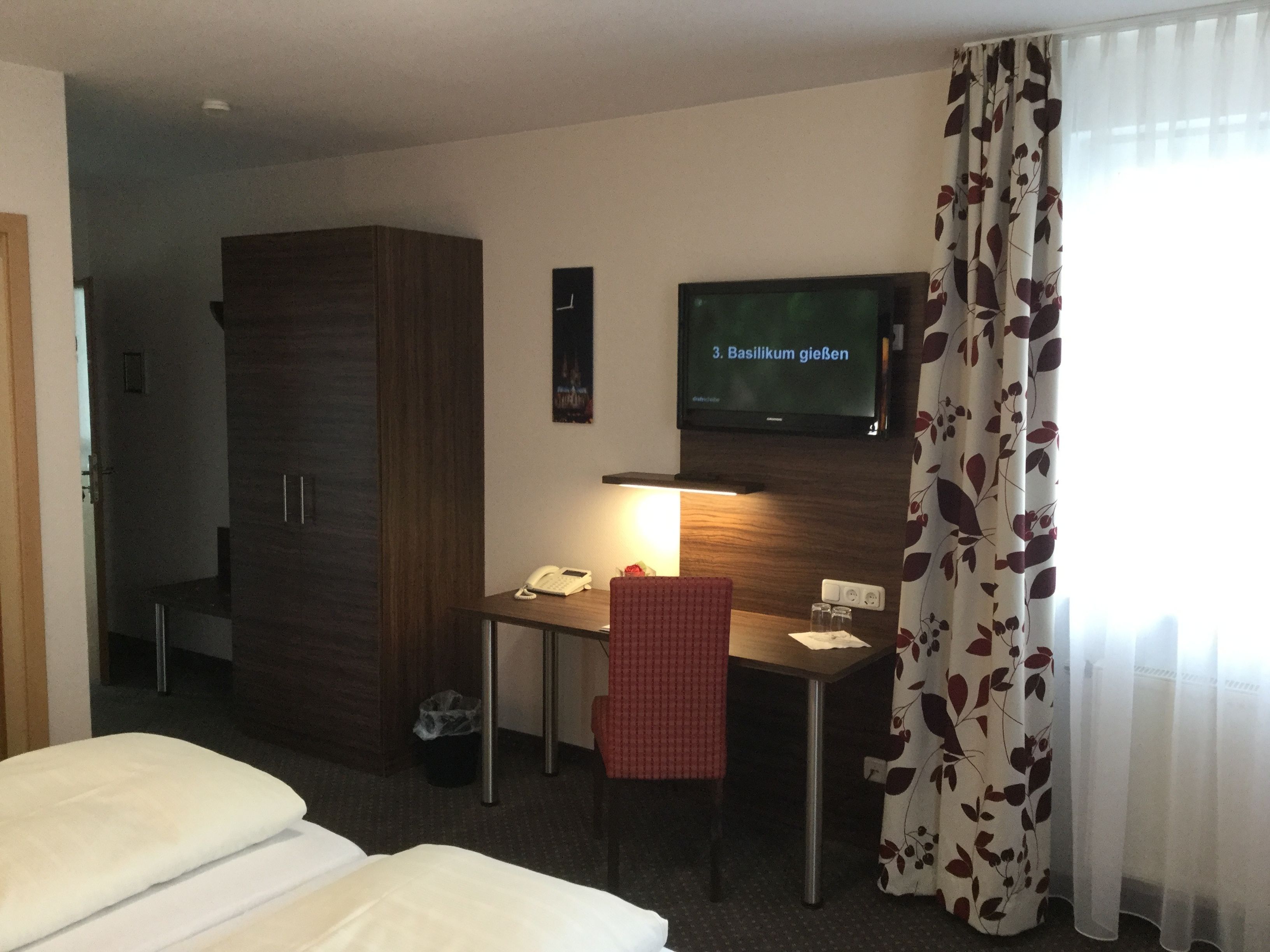 Ein Hotelzimmer mit einem Bett, einem Schreibtisch mit Telefon, einem Fernseher und einem Kleiderschrank.