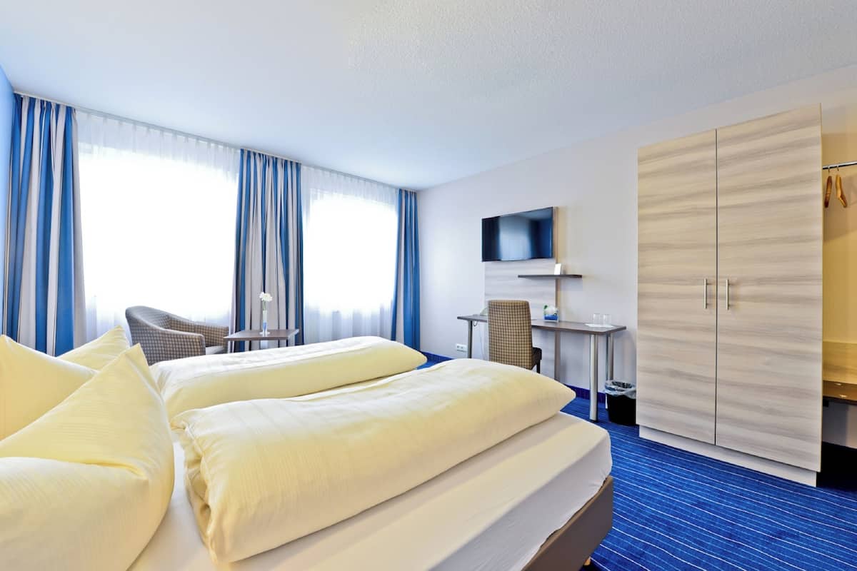 A hotel room with a large bed, a desk with a chair, a TV mounted on the wall, and a wardrobe.