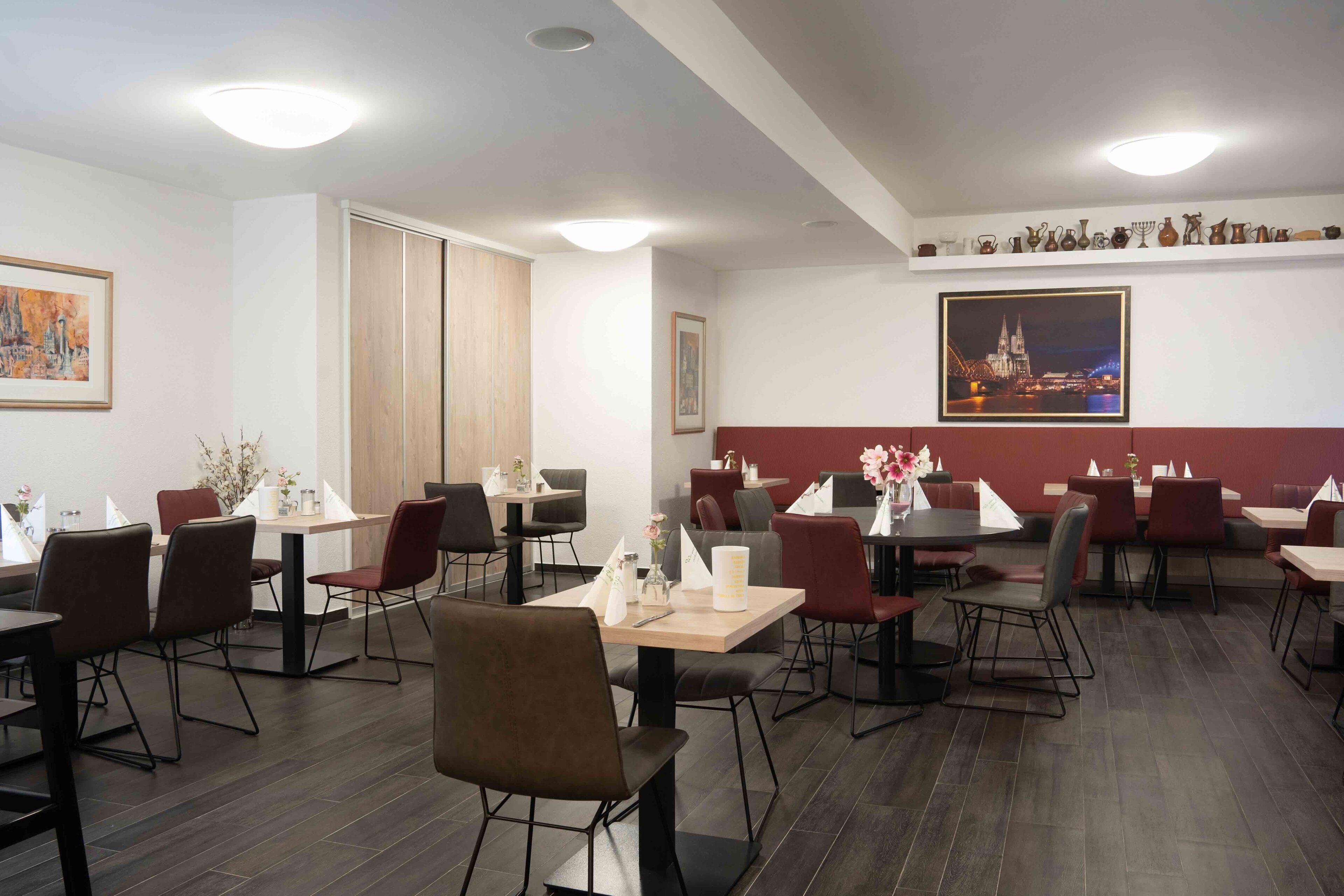 A restaurant with multiple tables and chairs, a wooden floor, and a wall with a framed picture and a shelf with various items.