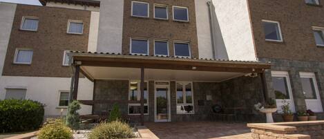 A multi-story building with a covered entrance, stone walls, and a courtyard with seating and plants.