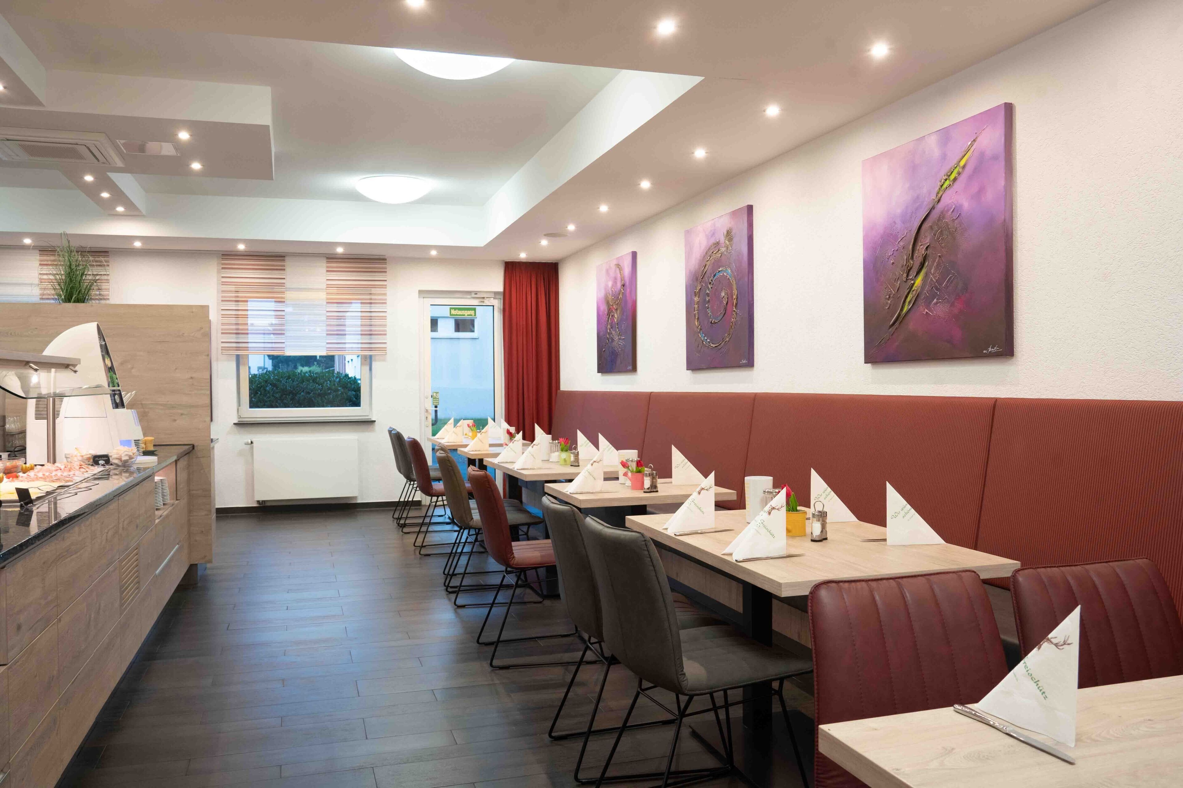 Un restaurante con mesas largas, cabinas acolchadas y obras de arte en las paredes.
