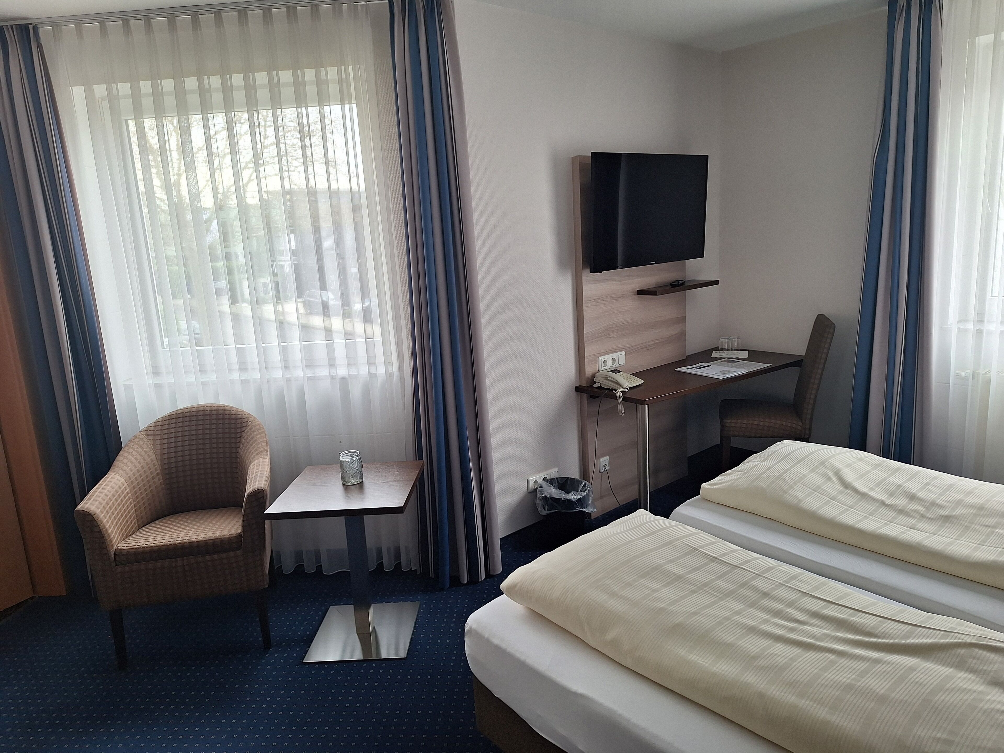 Een hotelkamer met een bed, een bureau, een stoel, een televisie en een raam met gordijnen.