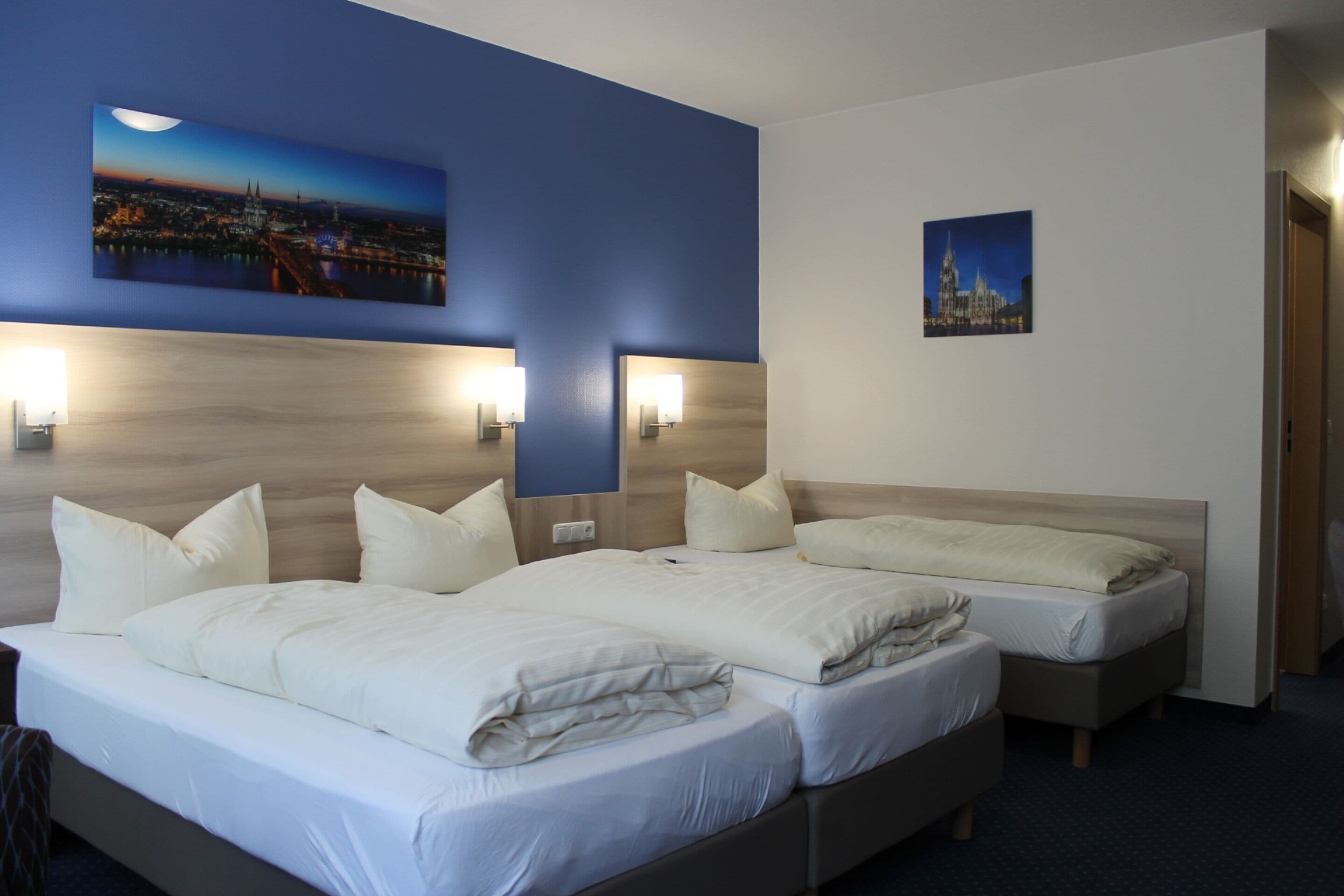 A hotel room with a large bed, two bedside tables, and a nightstand. There are two wall-mounted lamps and a framed picture on the wall.