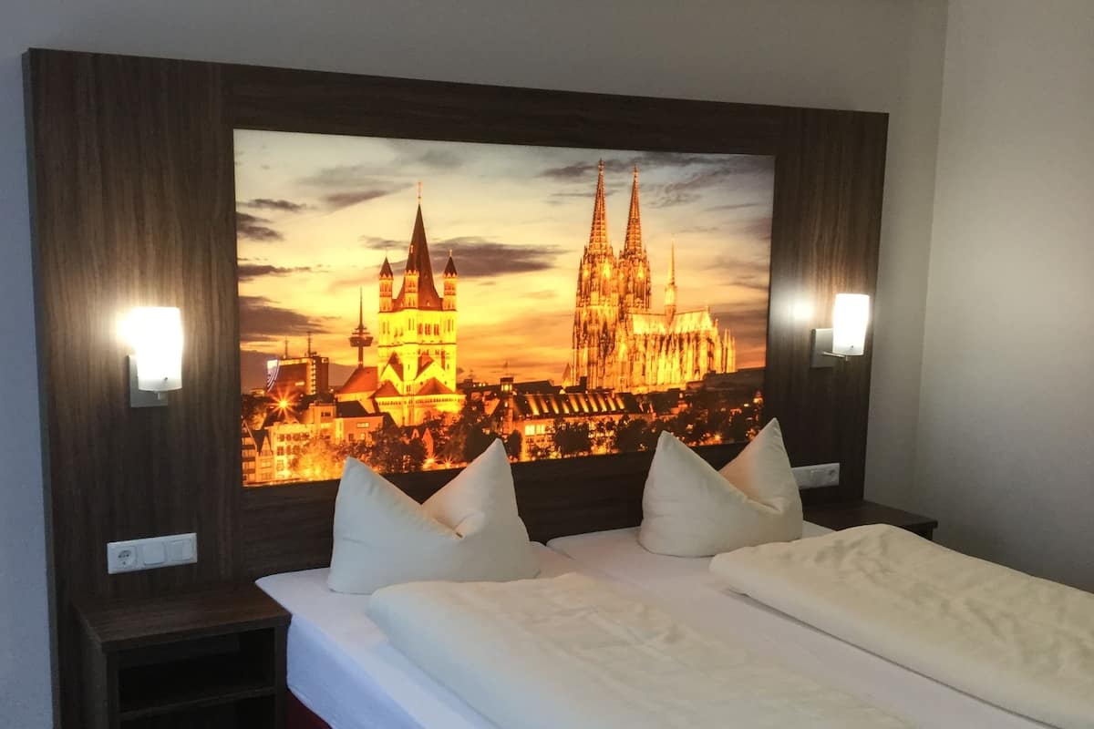 A hotel room with a large bed, two bedside tables, and a wall-mounted TV displaying a cityscape.