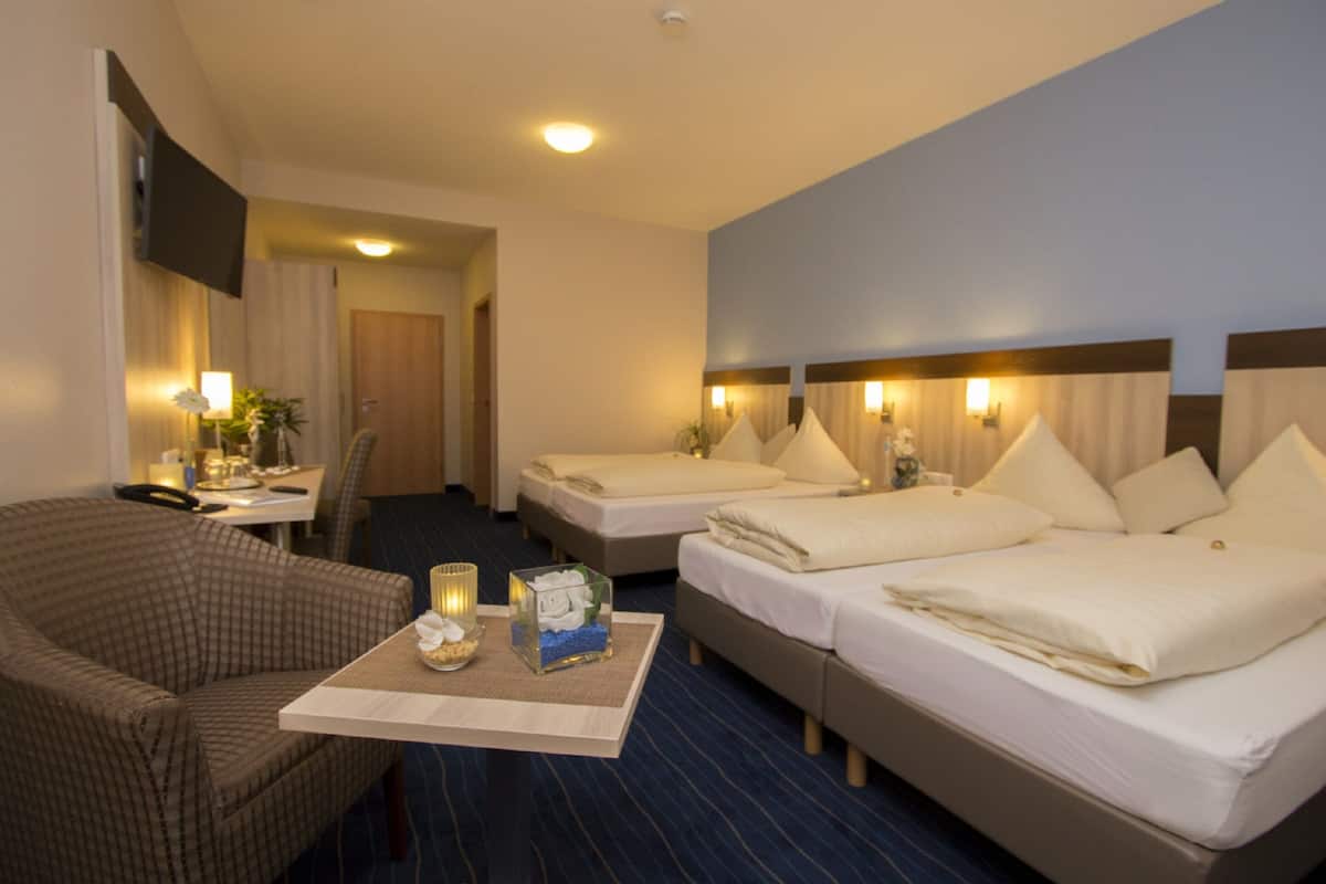 A hotel room with two beds, a desk with a chair, a flat-screen TV, and a small table with a candle and decorative items.