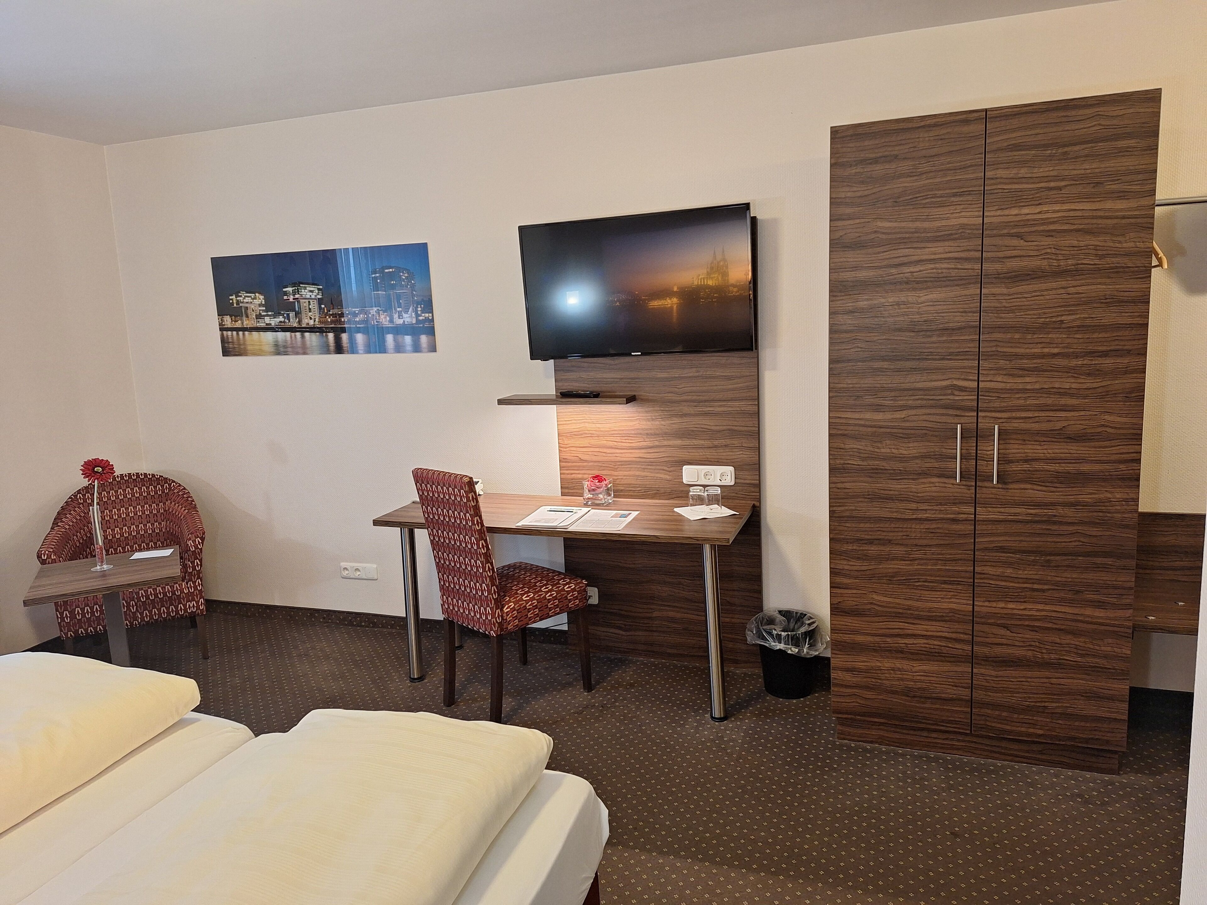 Una habitación de hotel con una cama, un escritorio con una silla, un televisor y un armario.