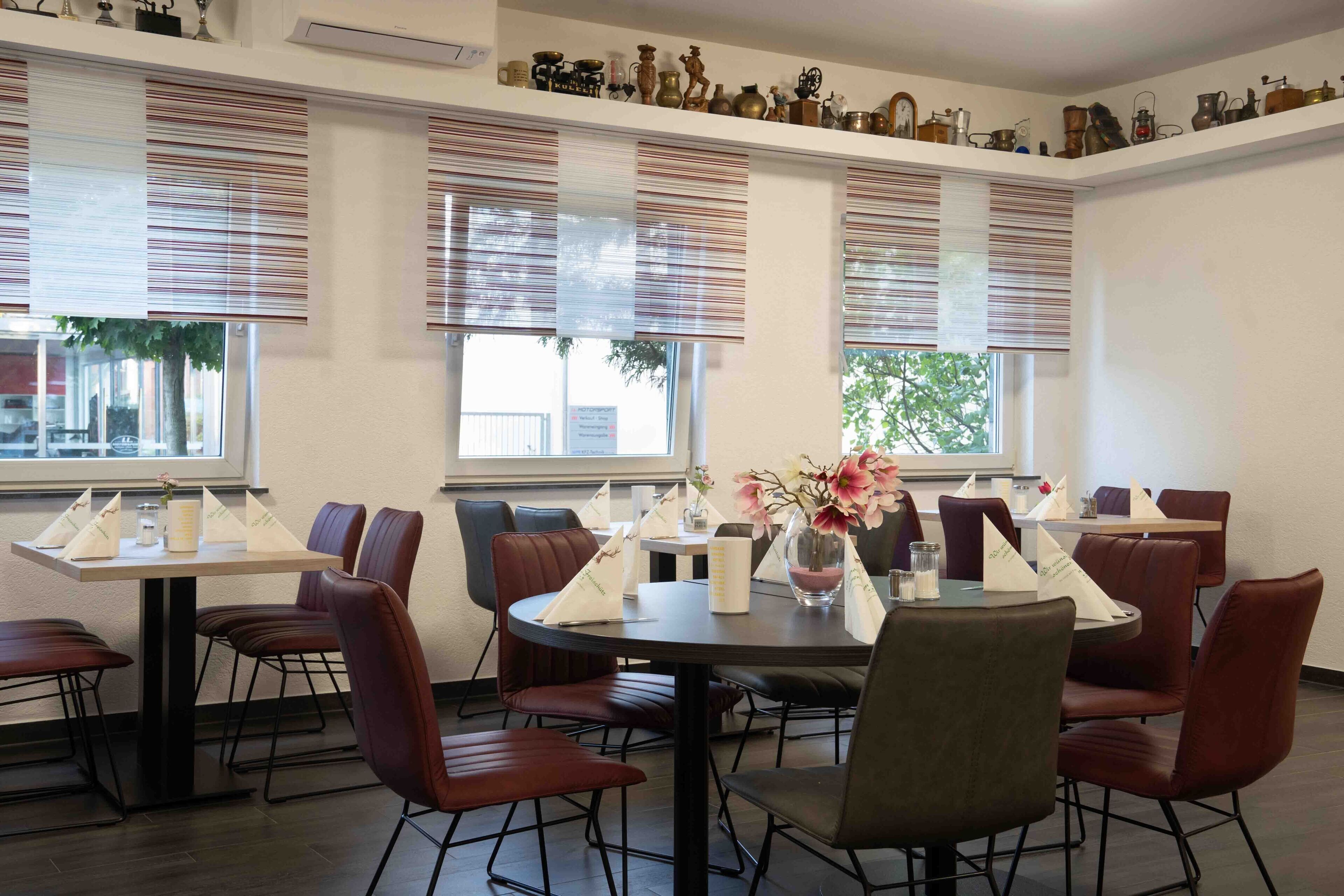 A dining area with round tables and chairs, large windows with blinds, and a variety of decorative items on the walls.