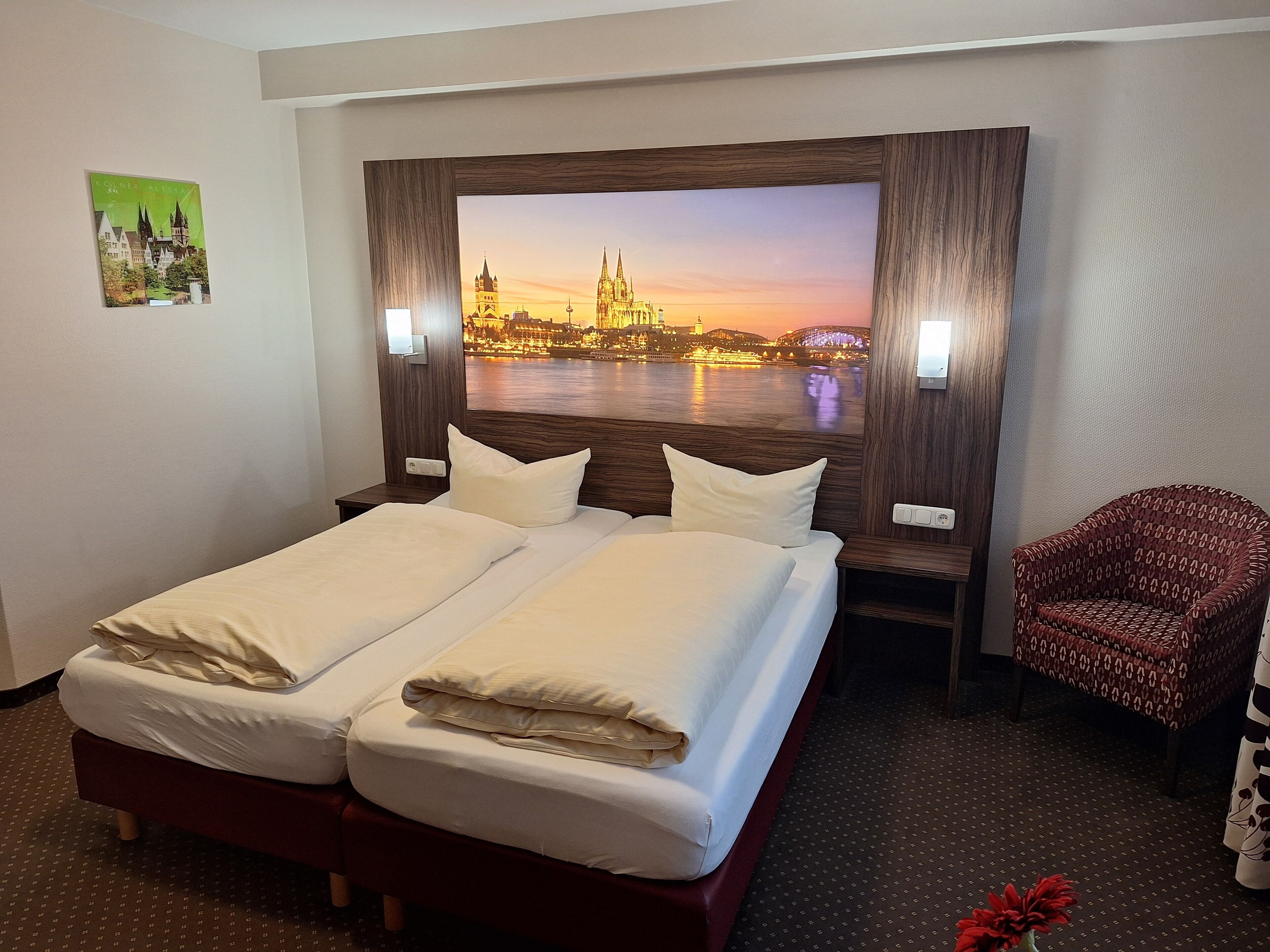 A hotel room with a large bed, two bedside tables, a chair, and a wall-mounted TV displaying a cityscape.