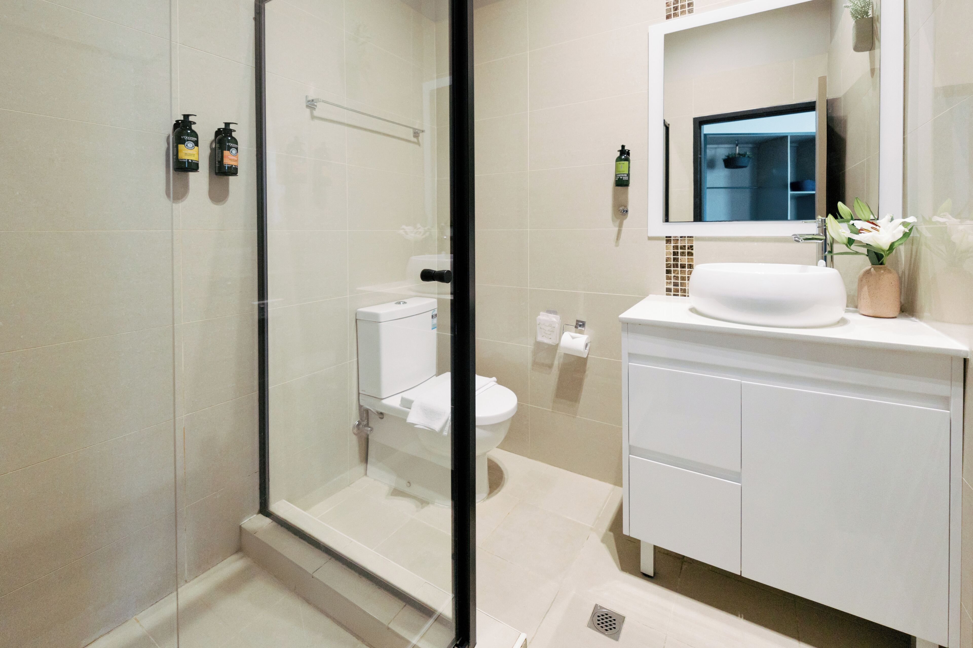 A modern bathroom with a glass shower enclosure, a white toilet, and a sink with a mirror above it.