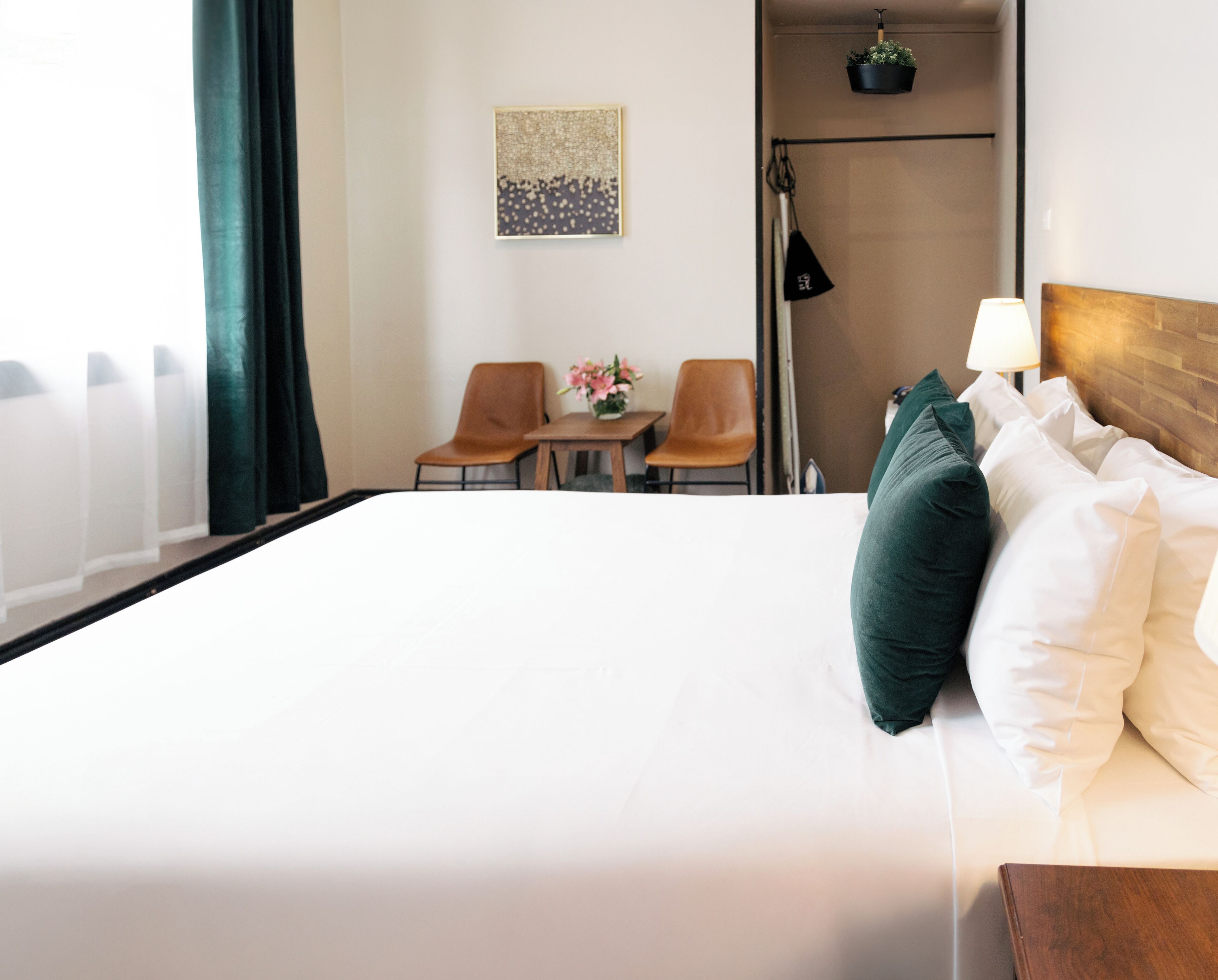Une chambre d’hôtel avec un grand lit, deux chaises, une petite table, une lampe, un tableau au mur et une plante en pot.