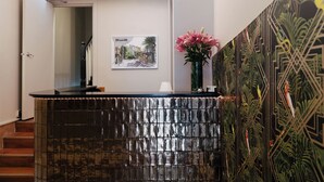 Una recepción con un cuadro de un paisaje urbano enmarcado, un jarrón con flores rosadas y un papel tapiz estampado.