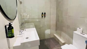 Een moderne badkamer met een douchecabine van glas, een witte wastafel met zeepdispenser en een toilet.