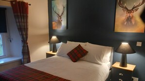A bedroom with a bed, two bedside tables, a lamp on each, a plaid blanket, and a window with curtains. - The Luib Hotel (Crianlarich)