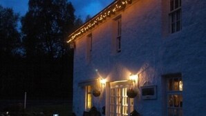 A building with a porch, a hanging lantern, and a lighted window. - The Luib Hotel (Crianlarich)